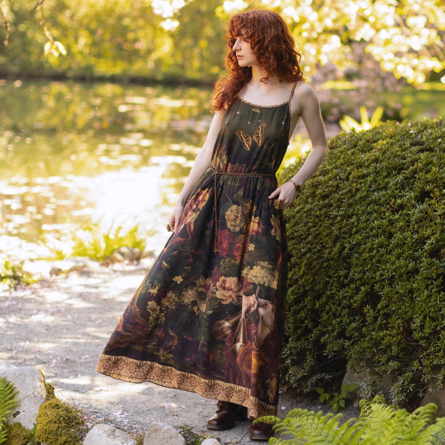 A woman standing on a path by a lake while wearing the The Messenger Long Maxi Slip Dress from Market Of Stars