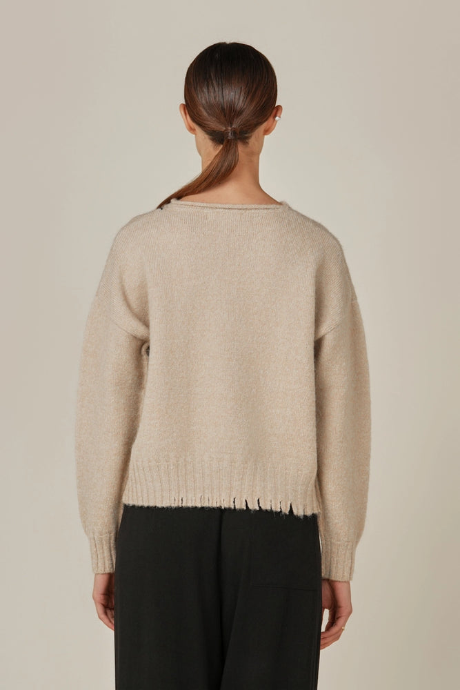 This women's pullover sweater features a relaxed fit with subtle distressing detail at the hem