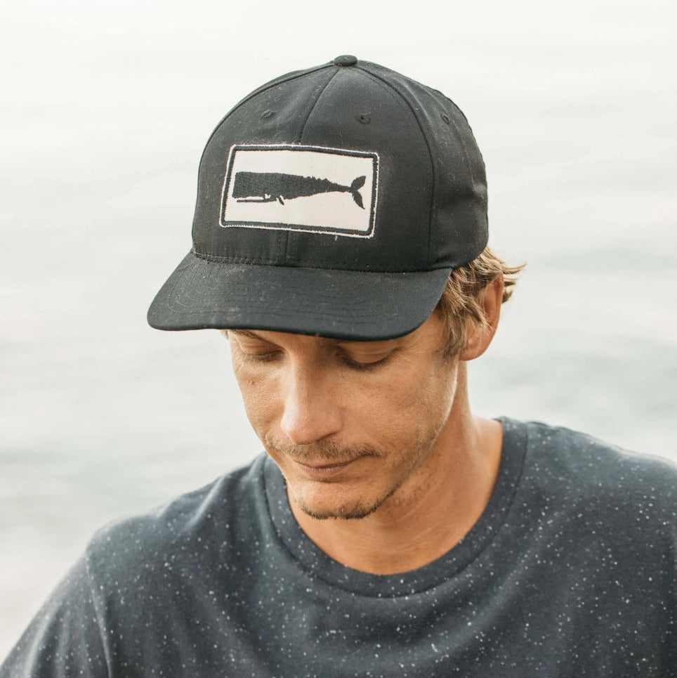 Man wearing a black cap with a whale patch
