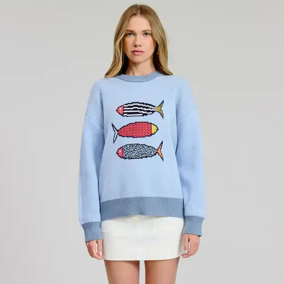 A woman wearing a blue pullover sweater from Flat White featuring a trio of multicolor sardines