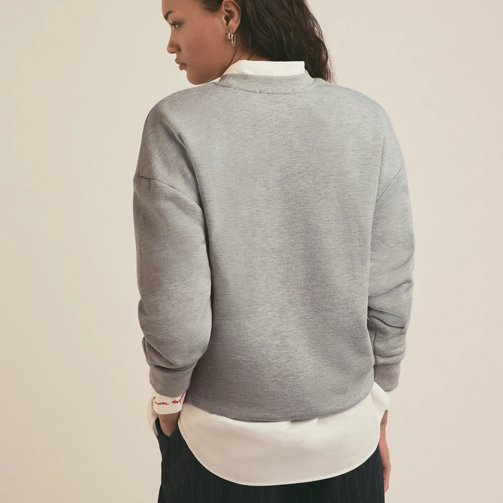 A woman wearing a grey crewneck sweatshirt from Favorite Daughter layered over a white collared shirt