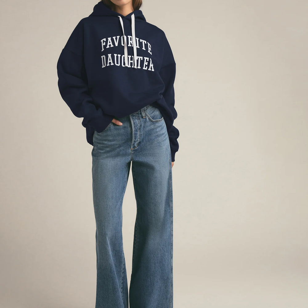 
                      
                        Person wearing a navy hoodie with 'FAVOURITE DAUGHTER' text and blue jeans on a beige background
                      
                    