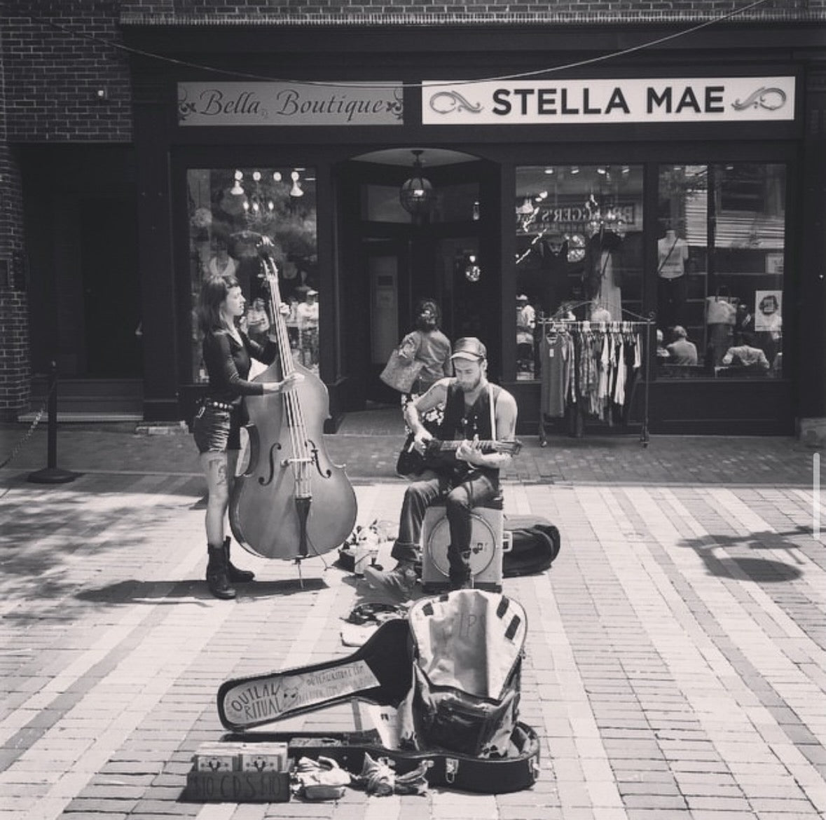 Street performer with musical instruments in front of a store named 'Stella Mae'.