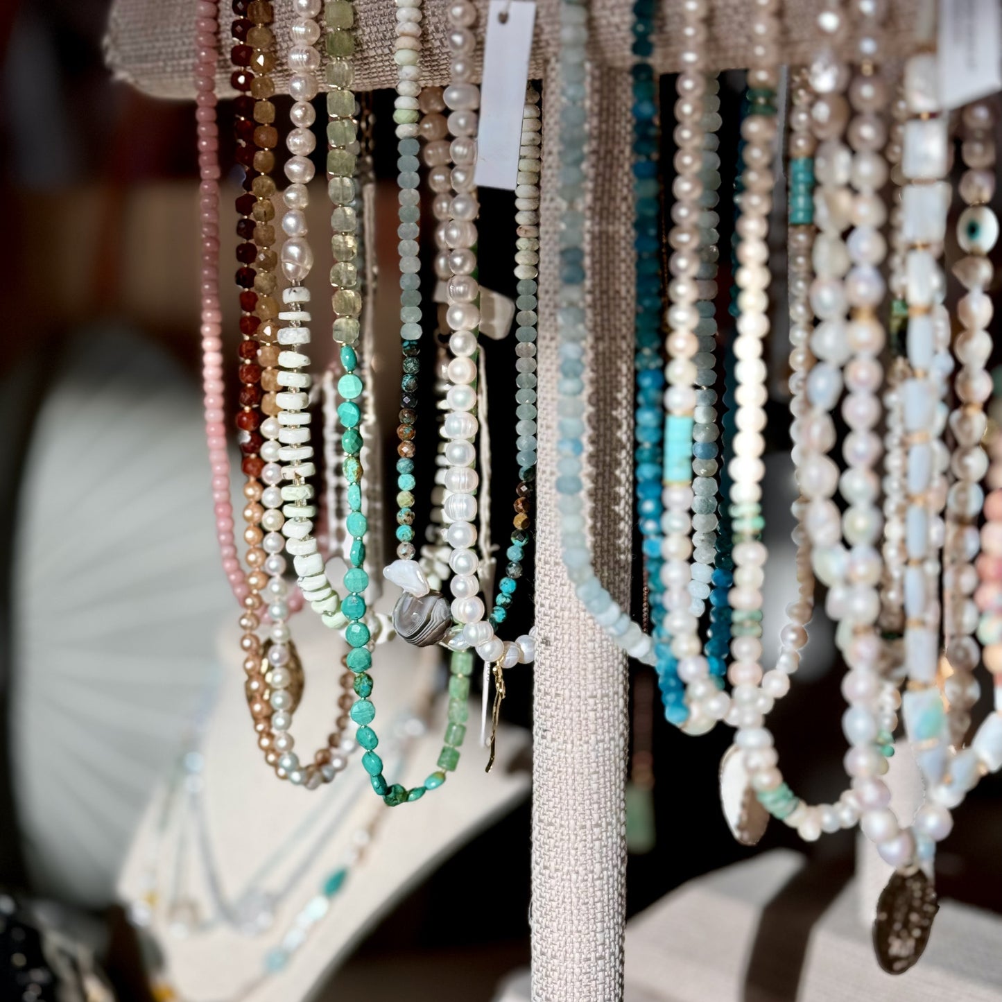 Display of various beaded necklaces on a stand with blurred background