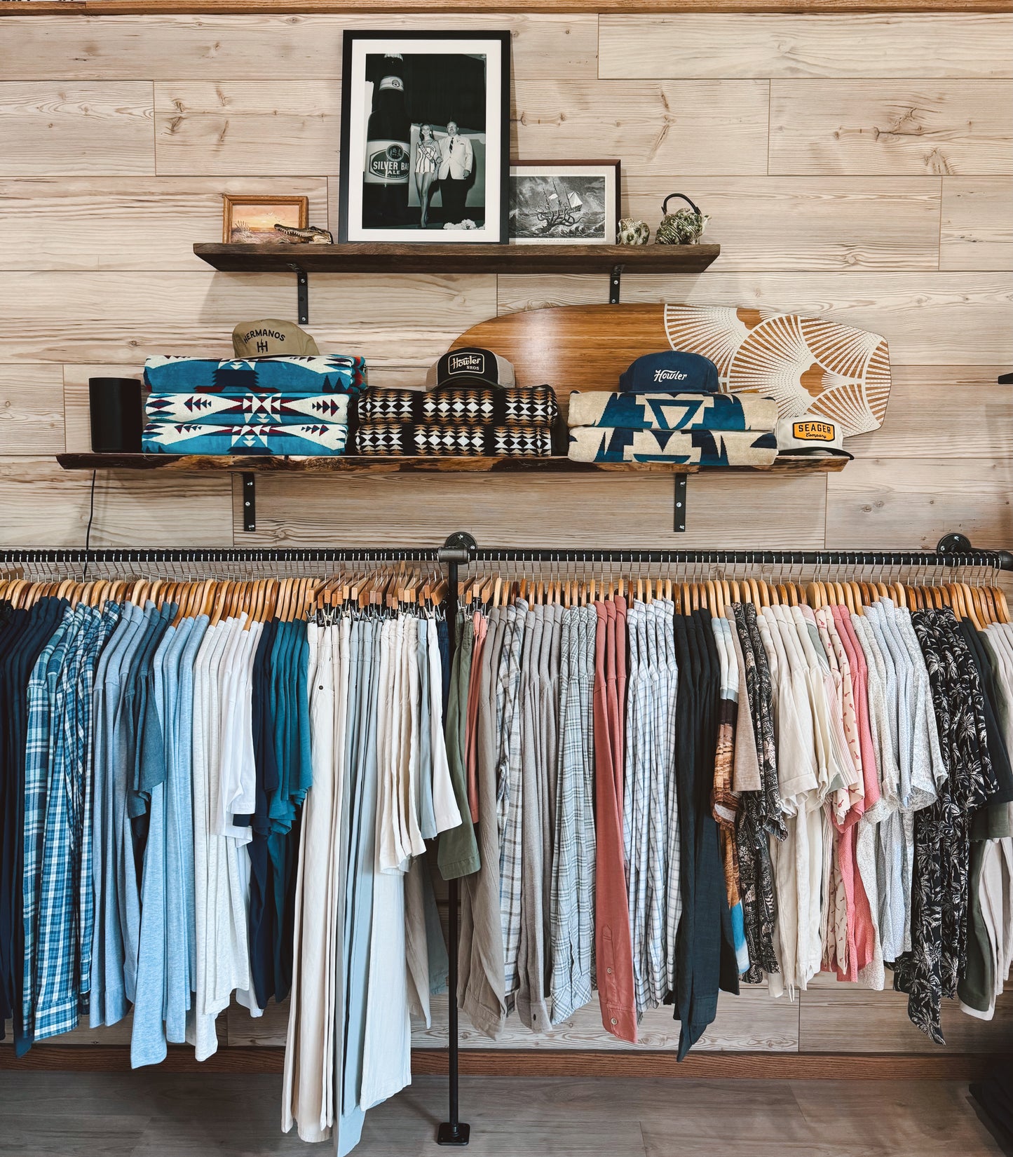 Clothing rack with shirts and pants against a wooden wall with shelves displaying accessories.