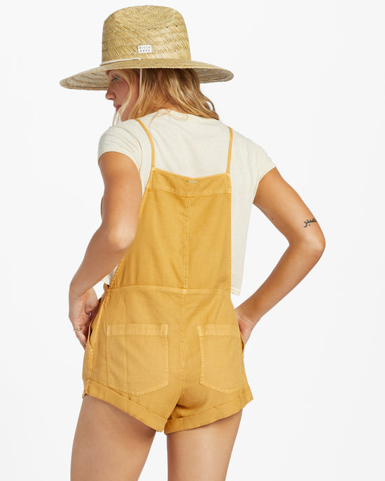 Back view view of model wearing a honey yellow color shorts romper by Billabong