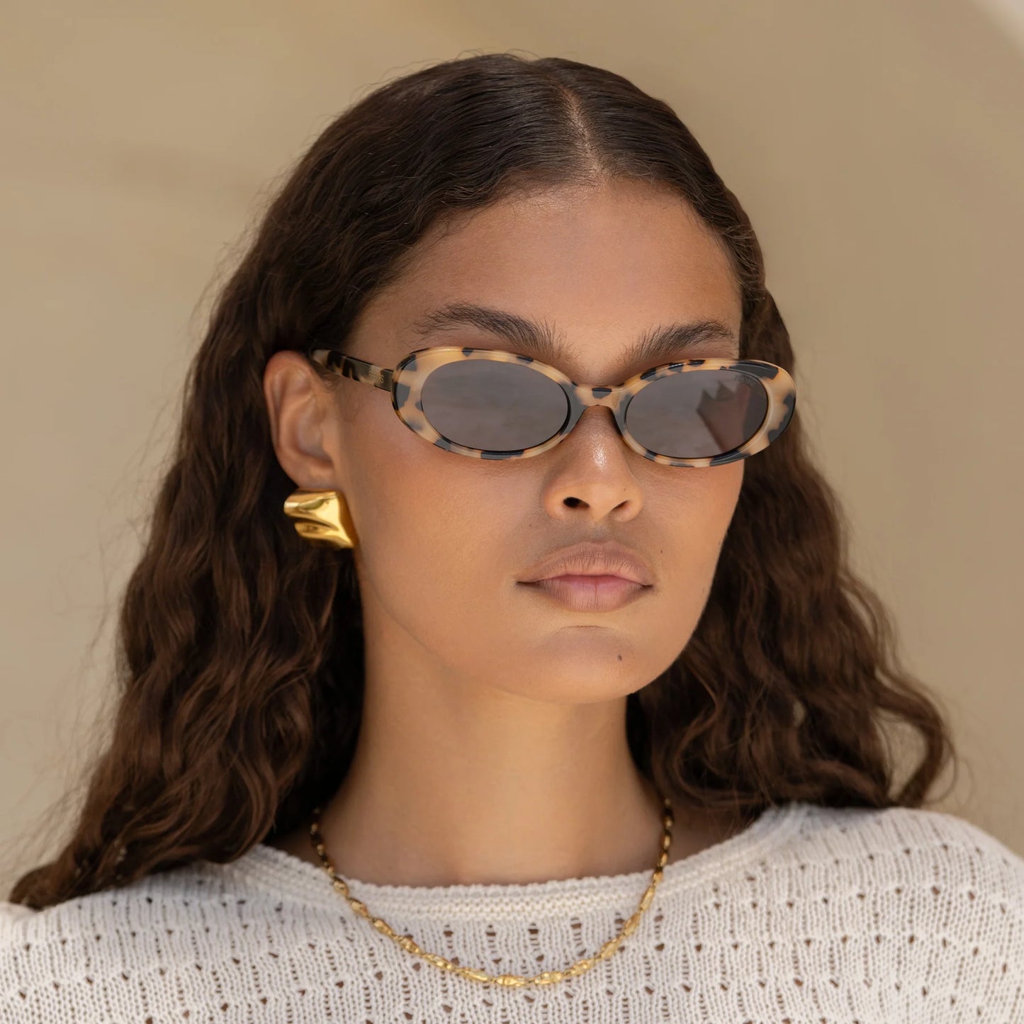 A woman wearing the FREYRS Mimi Women's Oval Sunglasses in the style Milky Tortoise