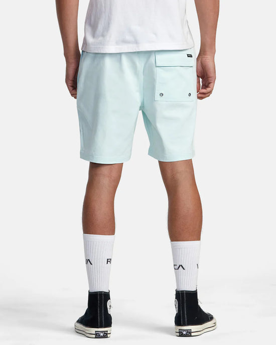Back view of man wearing light blue 17" walk shorts by RVCA with an elastic waistband and a back patch pocket