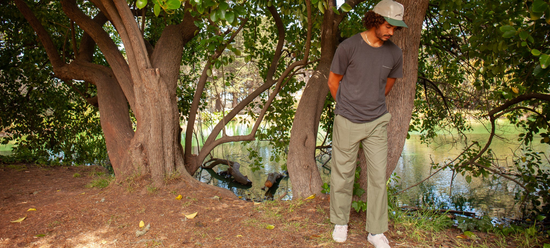 Man near water and trees wearing clothing from the brand Mollusk. 