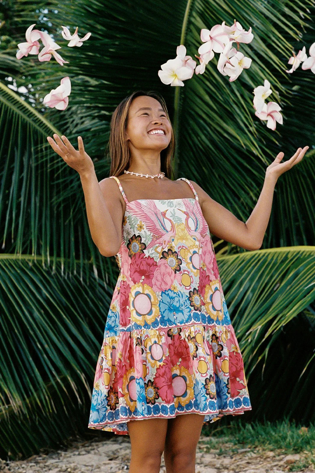 A woman outside wearing the Dancing Birds Scarlett Shift Mini Border Dress by Shore while throwing flower petals in the air