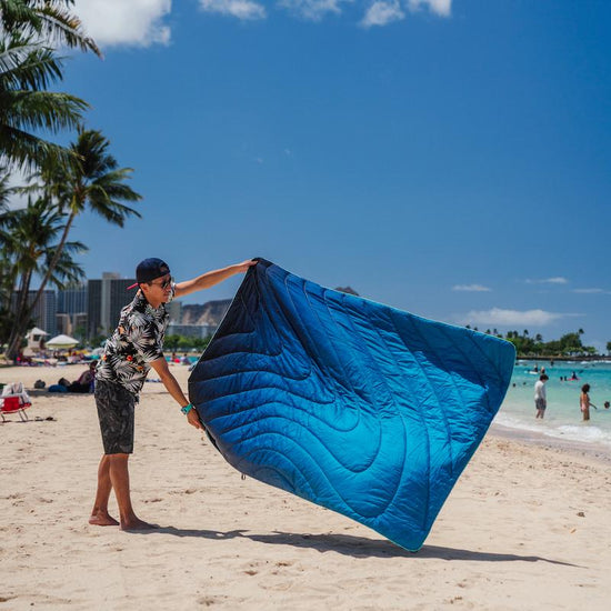 Man at the beach using Rumpl's Original Puffy Blanket (1 Person) in the color Ocean Fade