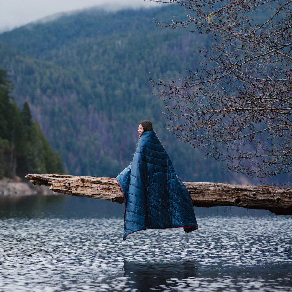 woman outside using Rumpl's Original Puffy Blanket (1 Person) in the color Deepwater