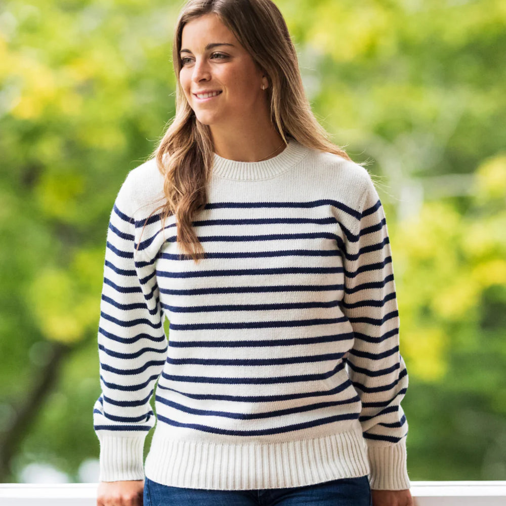 A woman standing on a porch while wearing the Women's 'Sconset SeaWell Sweater by Long Wharf Supply