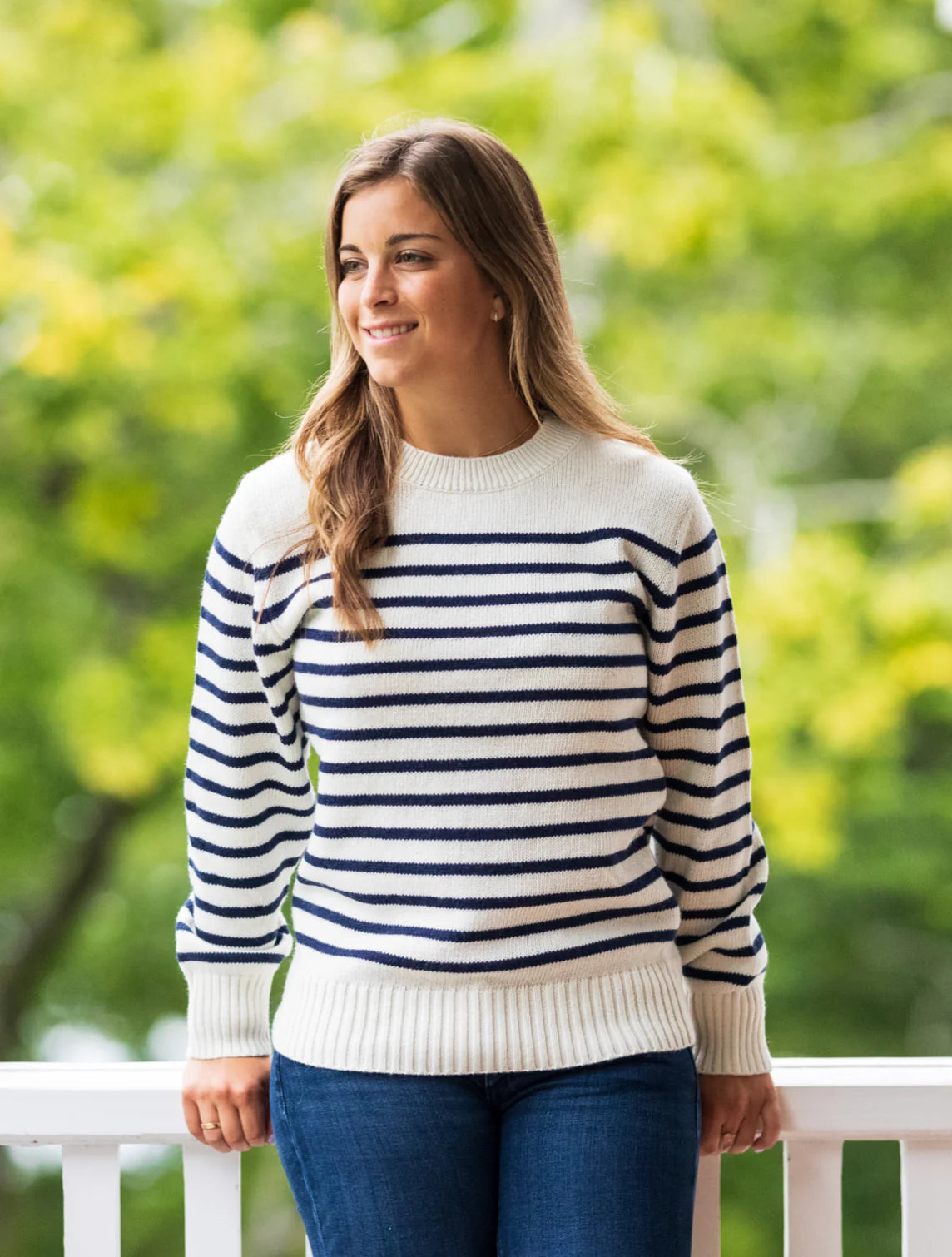 A woman standing on a porch while wearing the Women's 'Sconset SeaWell Sweater by Long Wharf Supply