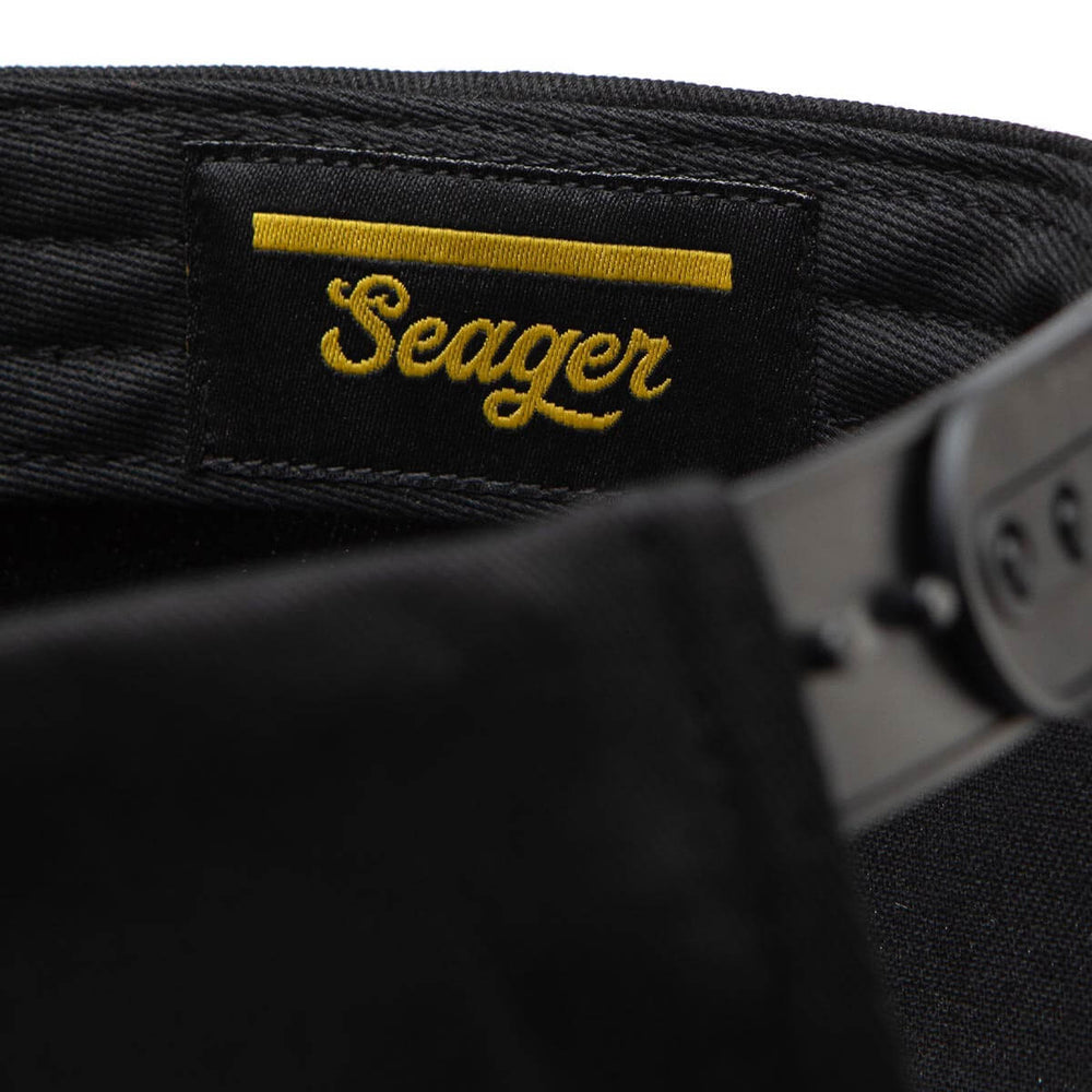 
                      
                        Close-up of a black hat with 'Seager' logo and snap closure.
                      
                    
