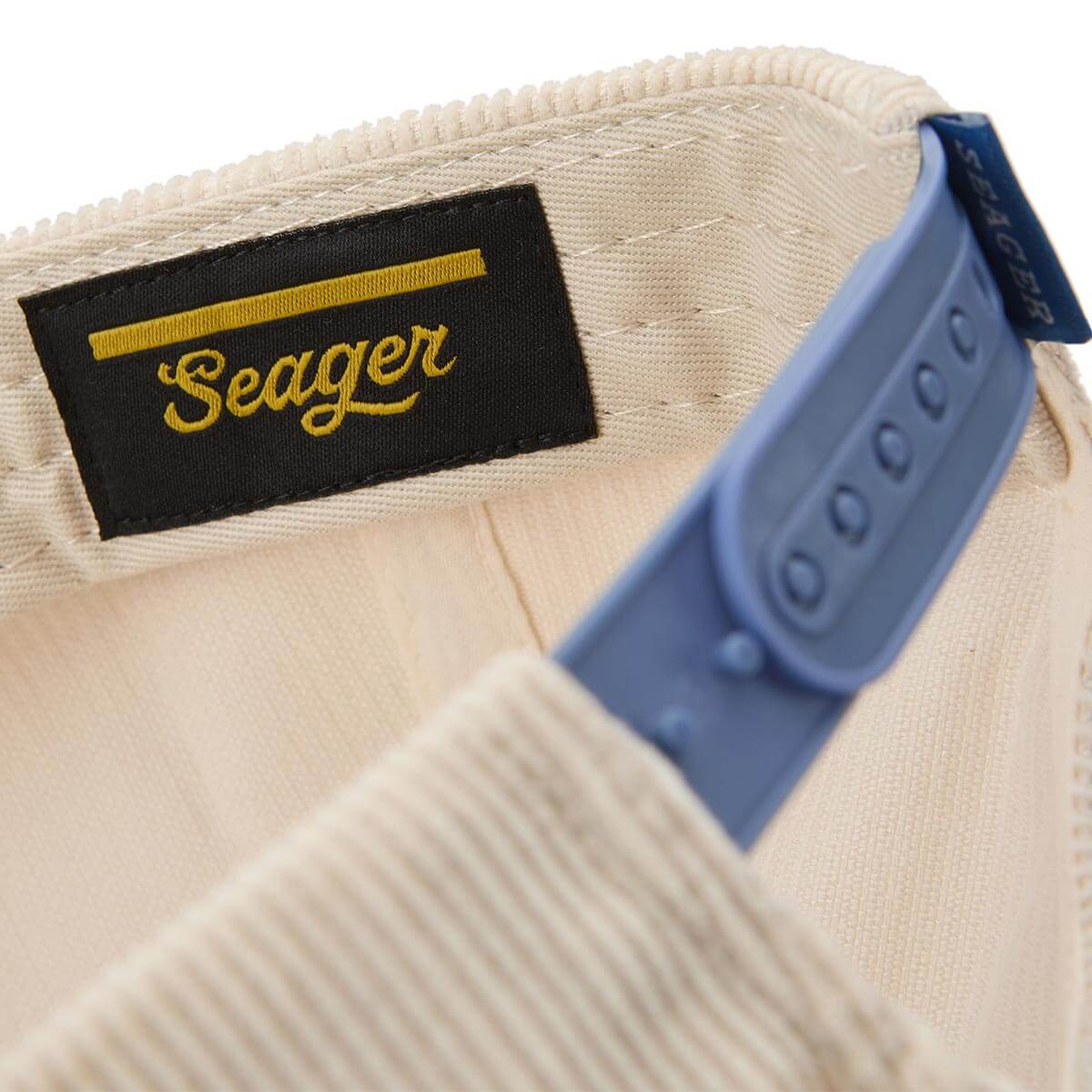 Close-up of a beige cap with a blue strap and 'Seager' logo