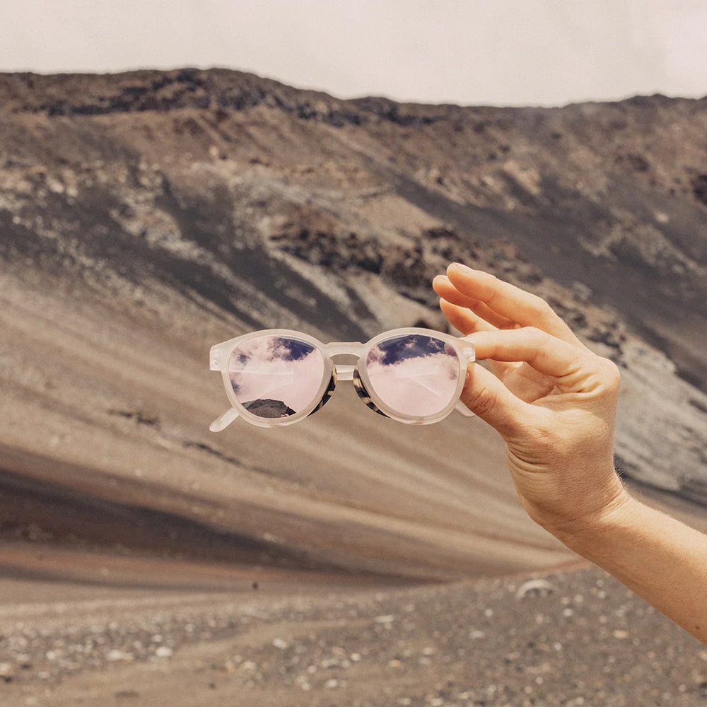 A person holding the Stone Alpenglow Tera Polarized Sunglasses by Sunski in front of a mountain