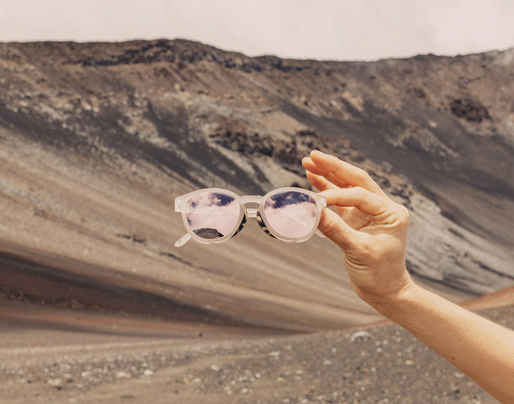 A person holding the Stone Alpenglow Tera Polarized Sunglasses by Sunski in front of a mountain