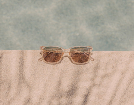 A pair of the Champagne Amber Ventana Polarized Sunglasses by Sunski sitting on the edge of a pool